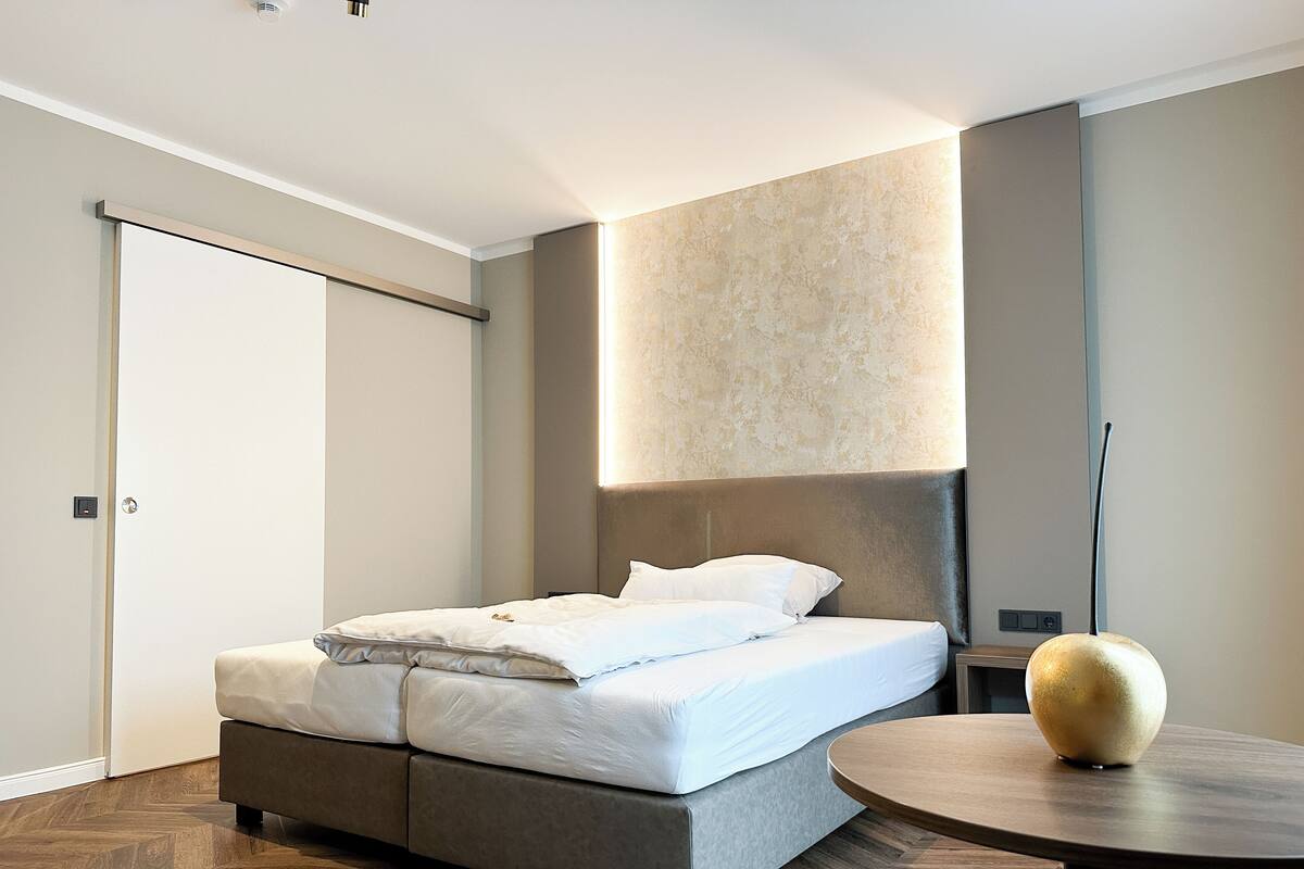 A modern bedroom with a bed, a round table, and a wall-mounted light fixture.