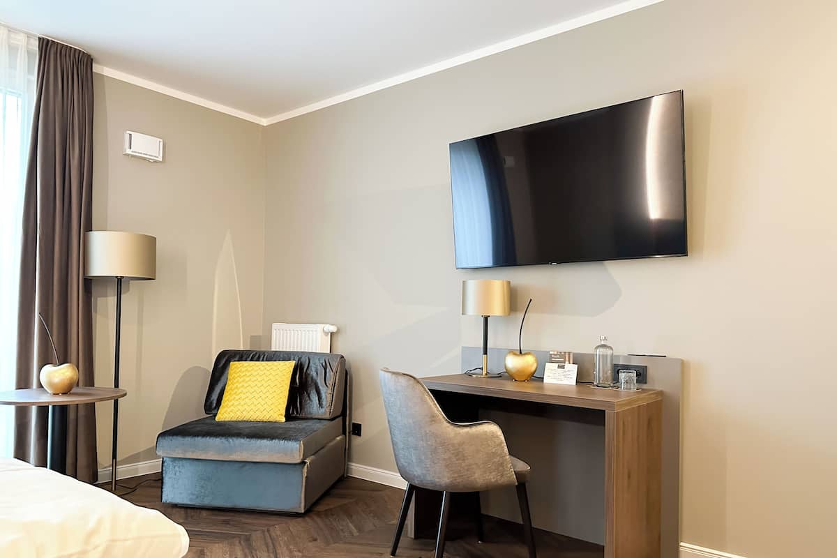 A hotel room with a bed, a desk with a chair, a television, and a lamp.