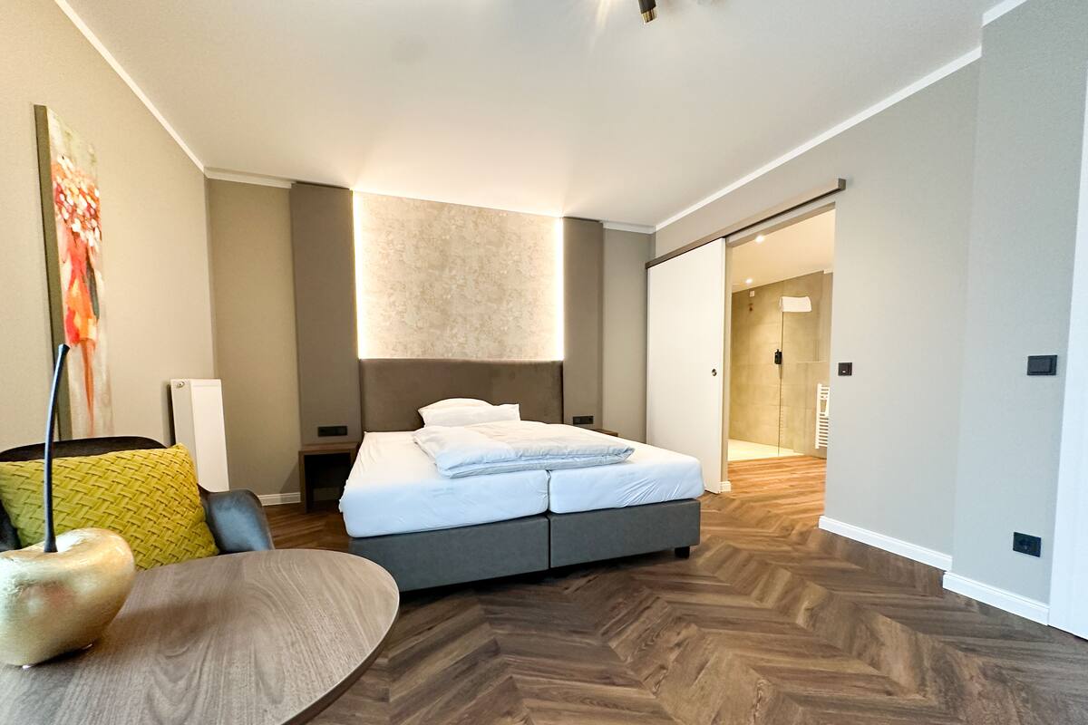 A modern hotel room with a bed, a round table, and a shower area.