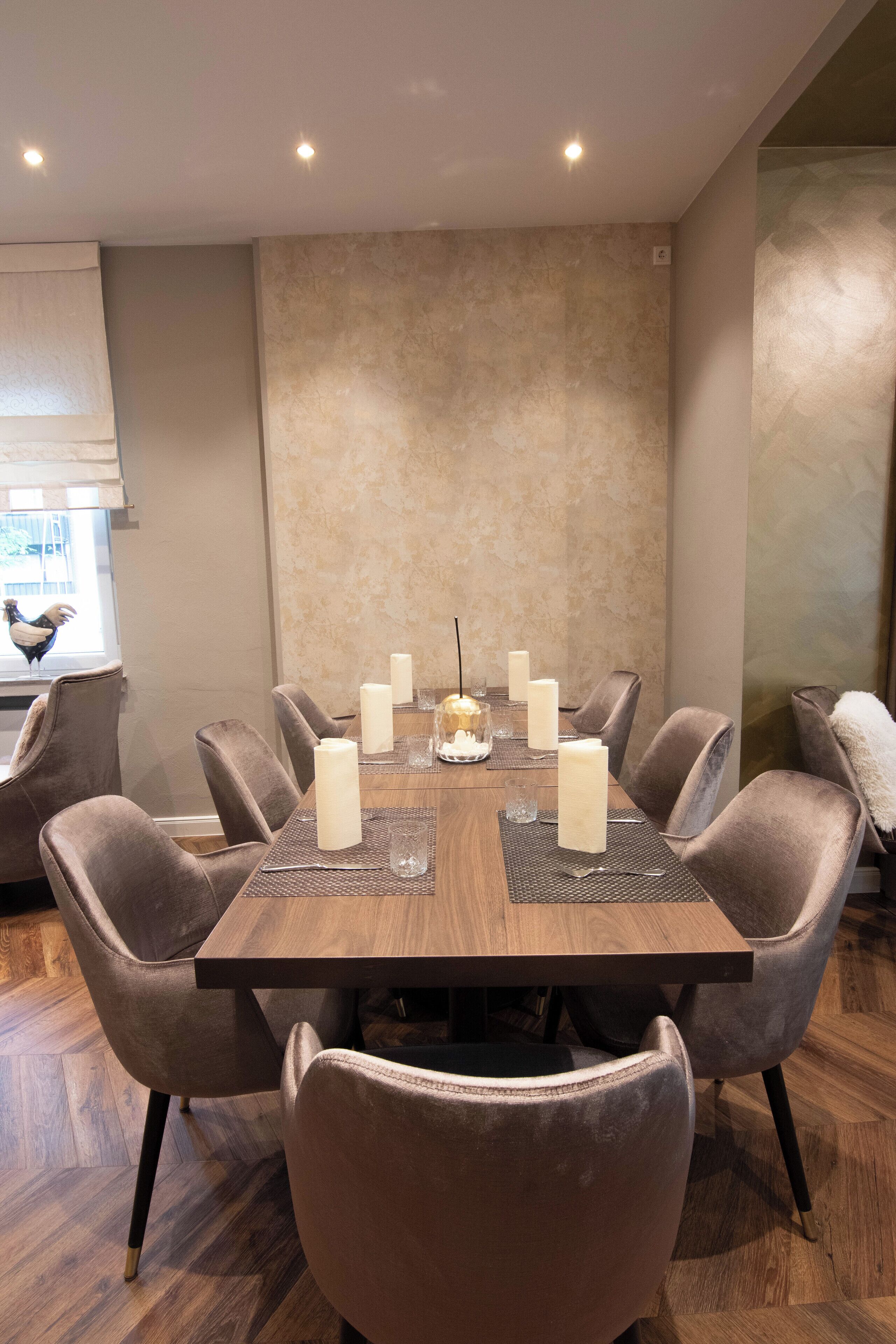 A dining area with a wooden table set for six, surrounded by six upholstered chairs.