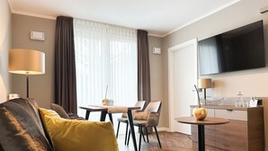 A modern hotel room with a sofa, a dining table, chairs, a TV, and a minibar. - Hotel Restaurant Hackmann-Atter (Osnabrueck)