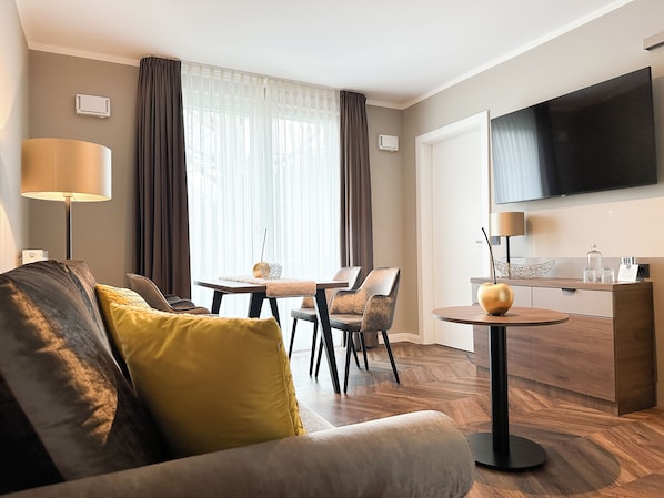 A modern hotel room with a sofa, a dining table, chairs, a TV, and a minibar. - Hotel Restaurant Hackmann-Atter (Osnabrueck)