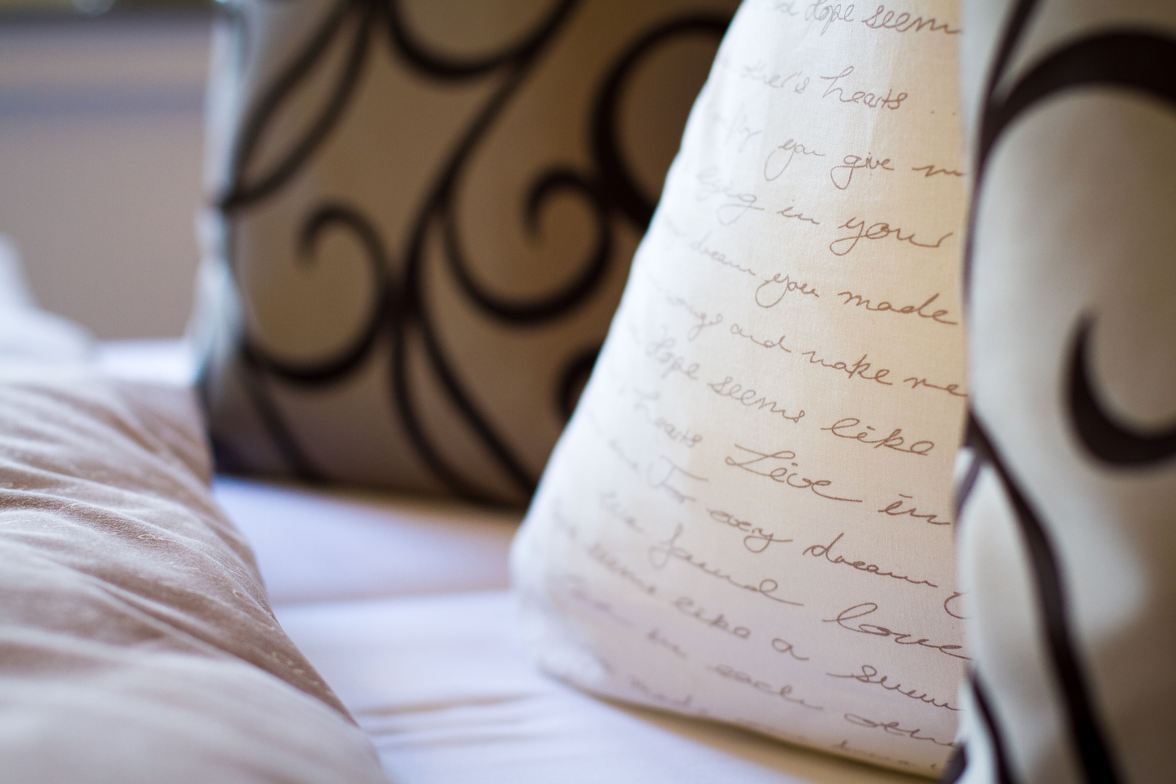 A close-up of a handwritten note on a pillow, a bed with a white cover, and a decorative metal headboard.