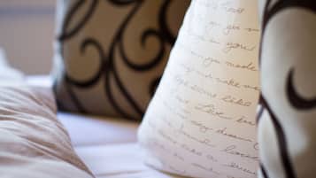 A close-up of a handwritten note on a pillow, a bed with a white cover, and a decorative metal headboard.