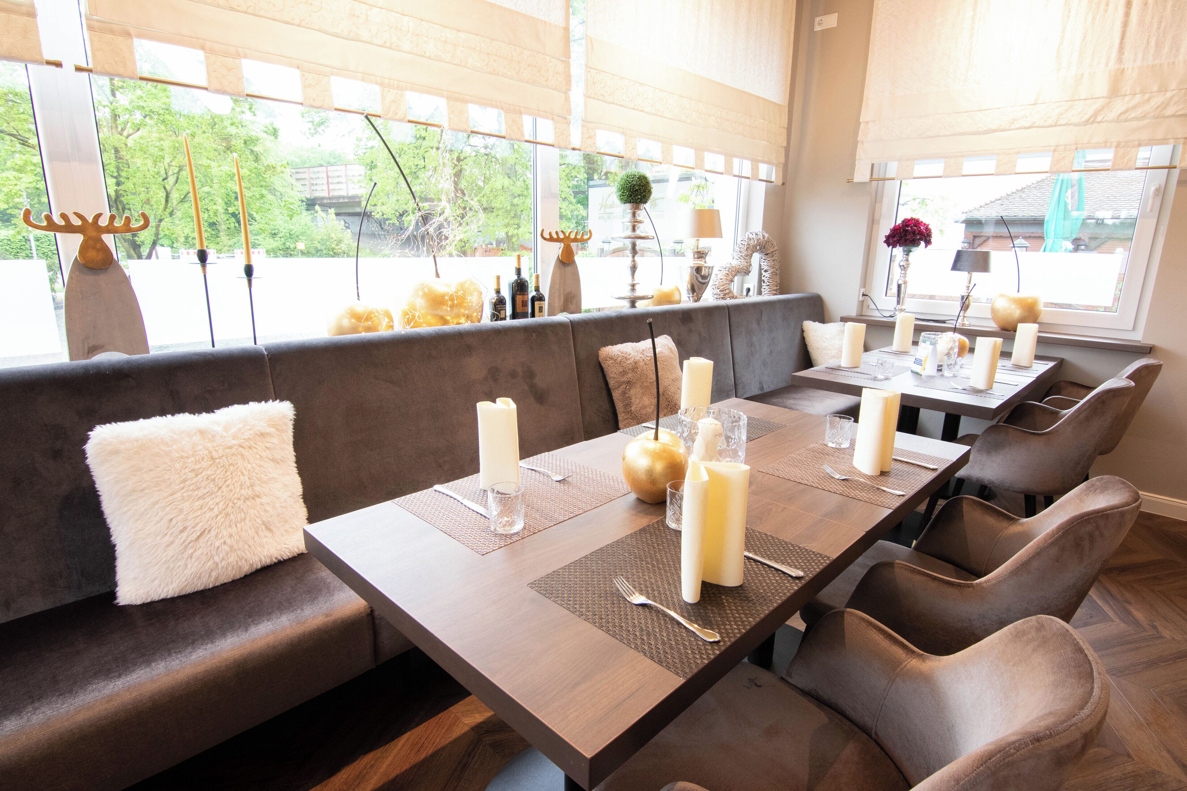Un restaurant doté d’une longue table en bois, préparée pour le repas, de sièges confortables et d’une vue dégagée grâce à de grandes fenêtres.