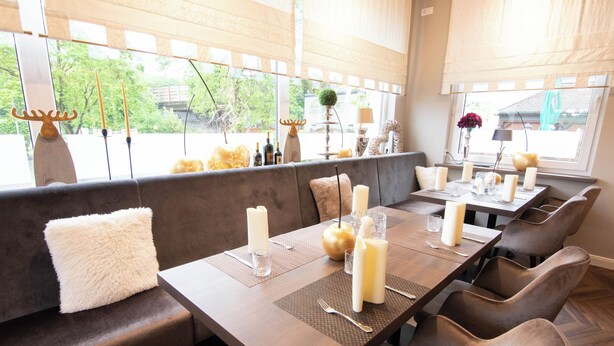 A restaurant with a long wooden table set for dining, cushioned seating, and a view through large windows. - Hotel Restaurant Hackmann-Atter (Osnabrueck)