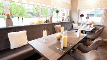 Un restaurant doté d’une longue table en bois, préparée pour le repas, de sièges confortables et d’une vue dégagée grâce à de grandes fenêtres.