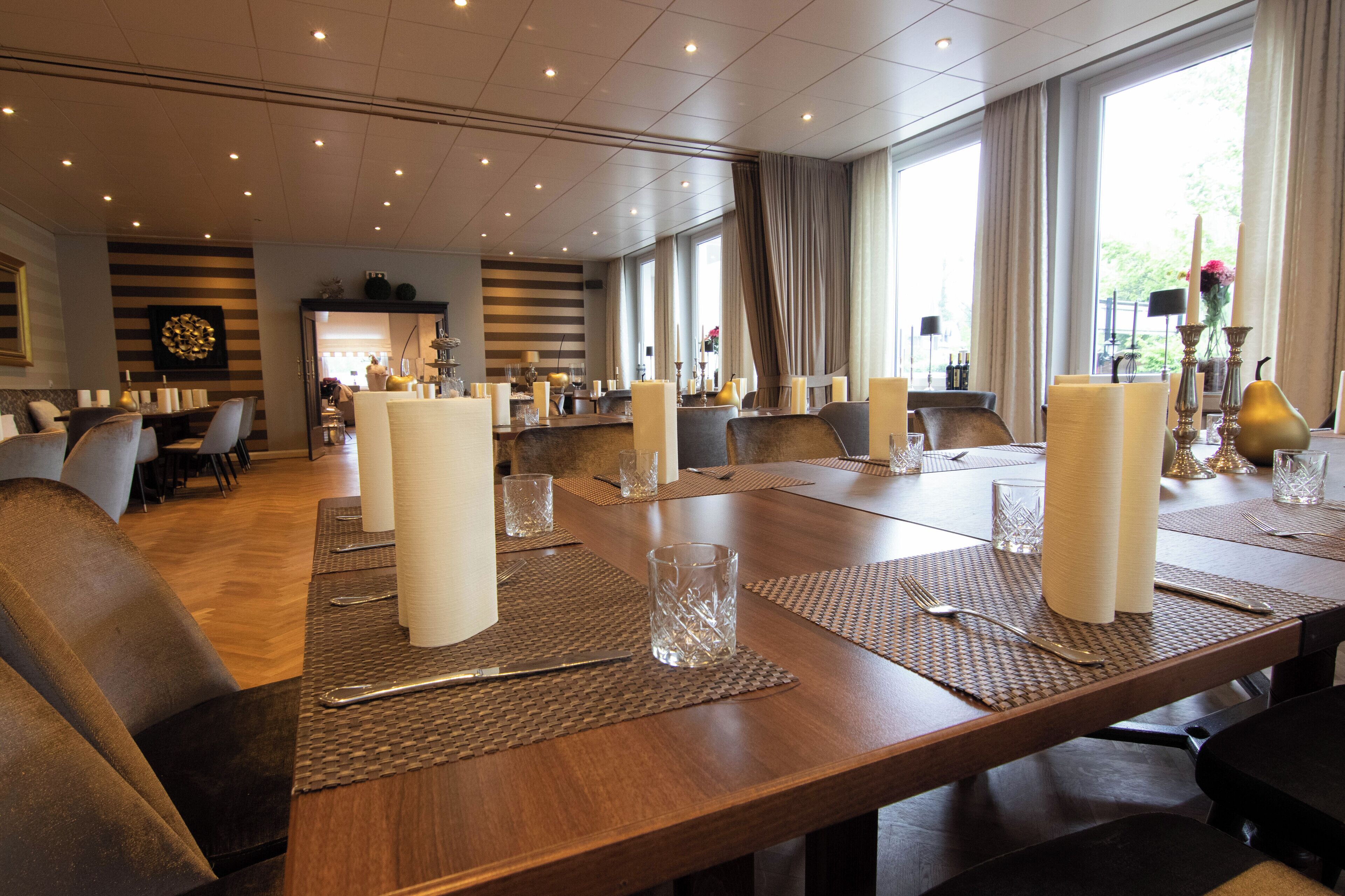 A conference room with a long table set for a meeting, surrounded by chairs, and large windows with curtains.