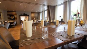 A conference room with a long table set for a meeting, surrounded by chairs, and large windows with curtains.