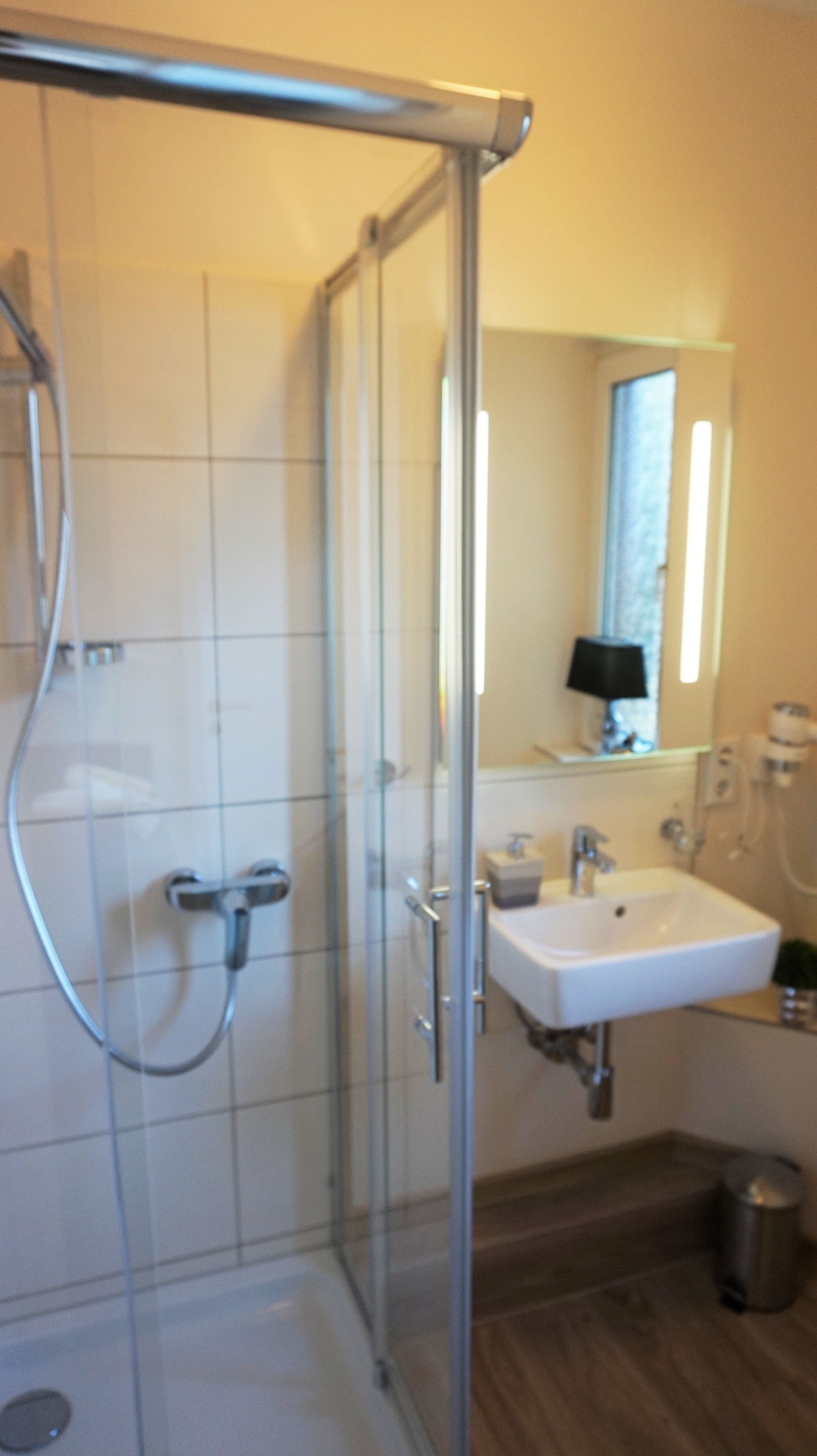 A bathroom with a glass shower enclosure, a white sink, and a mirror above the sink.