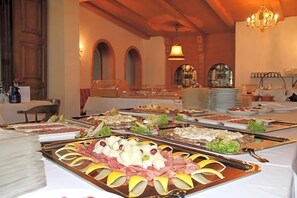 A buffet with various food items, a chandelier, and arched windows. - Hotel Hiemer (Memmingen)