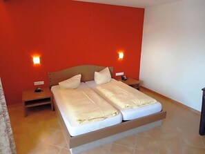 A double bed with a wooden headboard, two bedside tables, and a red accent wall. - Hotel Hiemer (Memmingen)