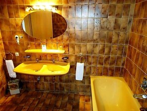 A bathroom with a yellow bathtub, two sinks, a mirror, and a towel rack. - Hotel Hiemer (Memmingen)