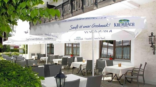 Ein Essbereich im Freien mit Tischen und Stühlen, beschattet von Sonnenschirmen, und ein Schild mit der Aufschrift 'Sanft ist unser Geschäft!'