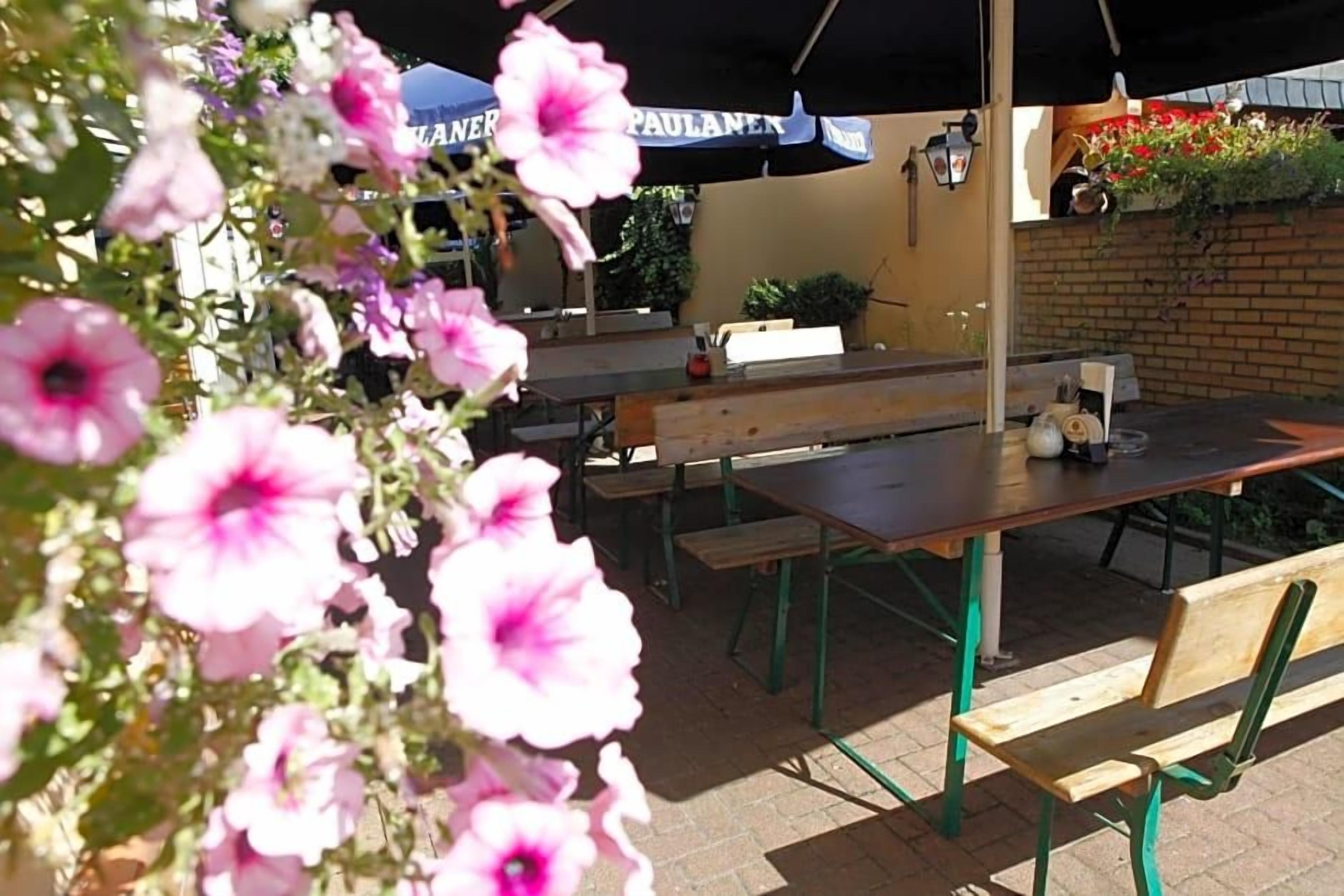 Un espace extérieur aménagé avec des tables, des bancs, des parasols et des fleurs.