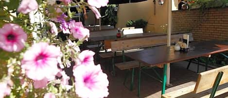 Un espace extérieur aménagé avec des tables, des bancs, des parasols et des fleurs.