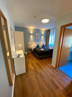 A hotel room with a bed, bedside table, and a desk with a lamp.