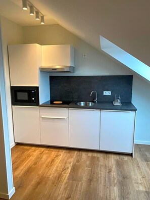 Une cuisine de taille réduite avec des meubles blancs, un four à micro-ondes, un évier et une cuisinière.