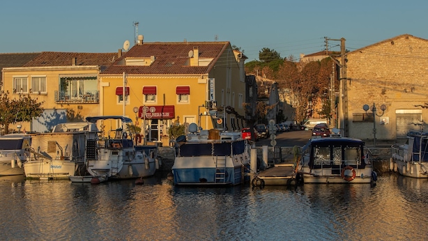 A marina with several boats docked, a building with a red awning, and a clear sky. - Logis Hotel Heraclee (Saint-Gilles)