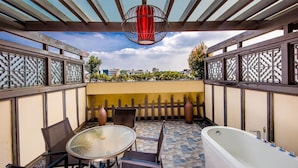 Un patio con una mesa y sillas de vidrio, una bañera blanca y un colgante decorativo rojo.