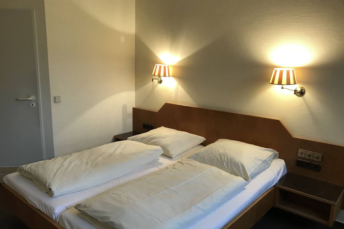 A double bed with white linens, two bedside lamps, and a wooden headboard.