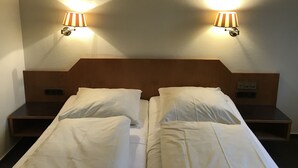 Ein Hotelzimmer mit zwei Betten, jeweils mit weißer Bettwäsche, und zwei Wandlampen mit gestreifter Lampenschirm.