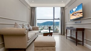 Una sala moderna con un sofá color beige, un reposapiés a juego, una mesa de centro de madera y un televisor montado en la pared.