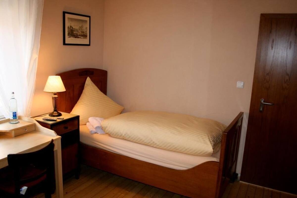 Une petite chambre à coucher, bien rangée, avec un lit simple, une table de chevet avec une lampe, une chaise et un bureau.