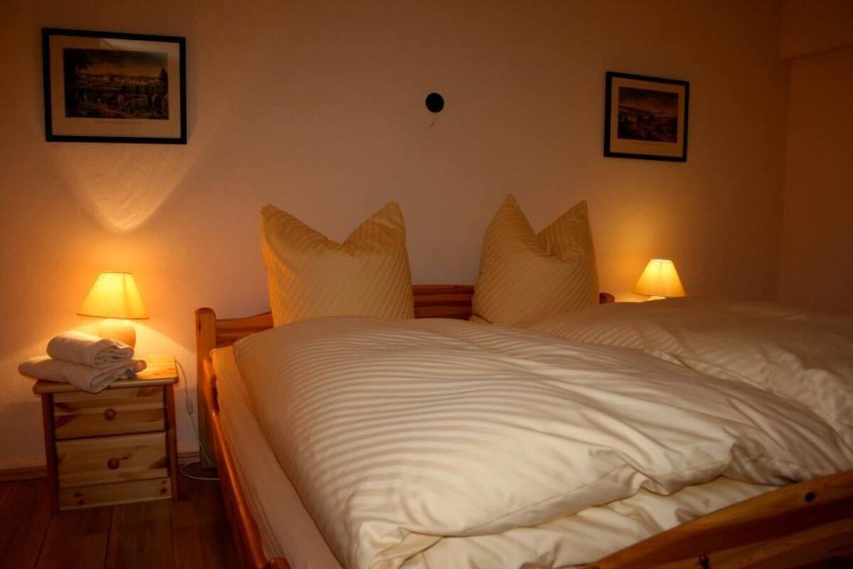 Un lit bien fait, avec des oreillers, une lampe de chevet et une table de nuit en bois sur laquelle est posée une serviette pliée.