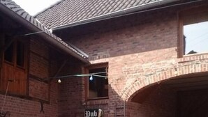 A brick building with a sign reading "Pub" above the entrance. There is a person standing in front of the pub, and a chalkboard with writing on it is visible to the left. - Mcmüllers Brauereigasthof (Linnich)
