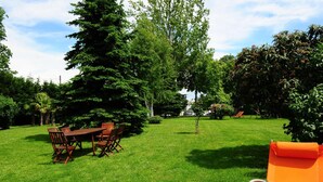 A grassy outdoor area with a wooden table and chairs, surrounded by trees and a clear sky. - Il Carrettino Country Hotel (Tortona)