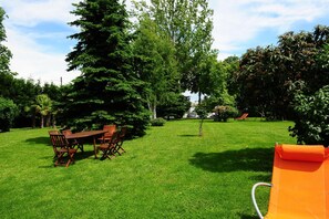 A grassy outdoor area with a wooden table and chairs, surrounded by trees and a clear sky. - Il Carrettino Country Hotel (Tortona)