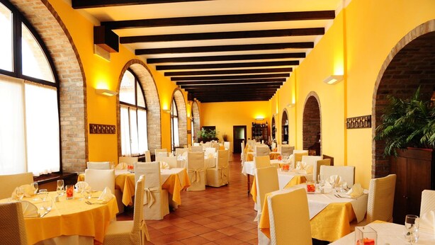 A restaurant with multiple tables set for dining, featuring a brick wall and arched windows. - Il Carrettino Country Hotel (Tortona)