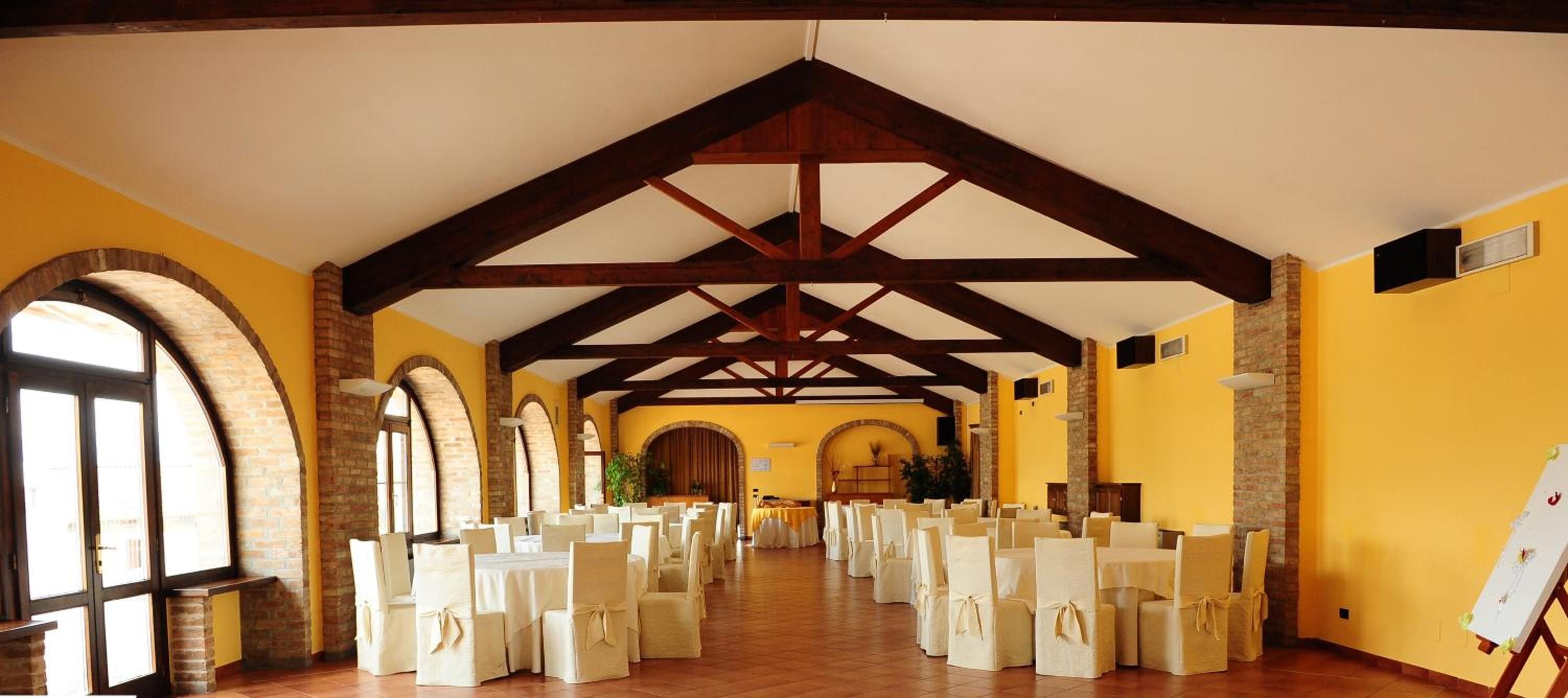 A spacious hall with a high ceiling, wooden beams, and brick arches. Tables and chairs are arranged for an event.