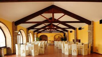 A spacious hall with a high ceiling, wooden beams, and brick arches. Tables and chairs are arranged for an event.