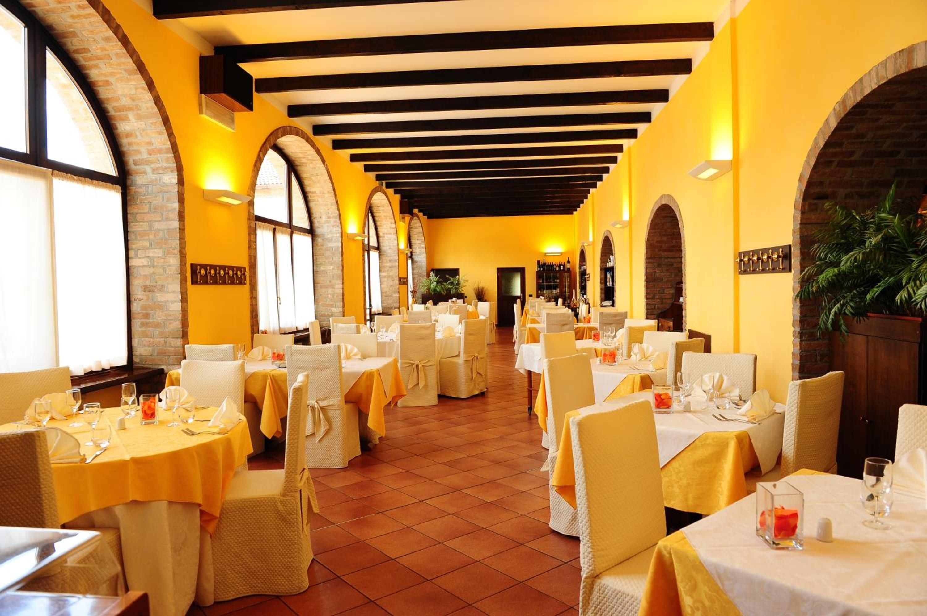 Een restaurant met meerdere tafels gedekt voor diners, met een bakstenen muur en rondboogvensters.
