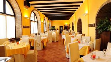 A restaurant with multiple tables set for dining, featuring a brick wall and arched windows.