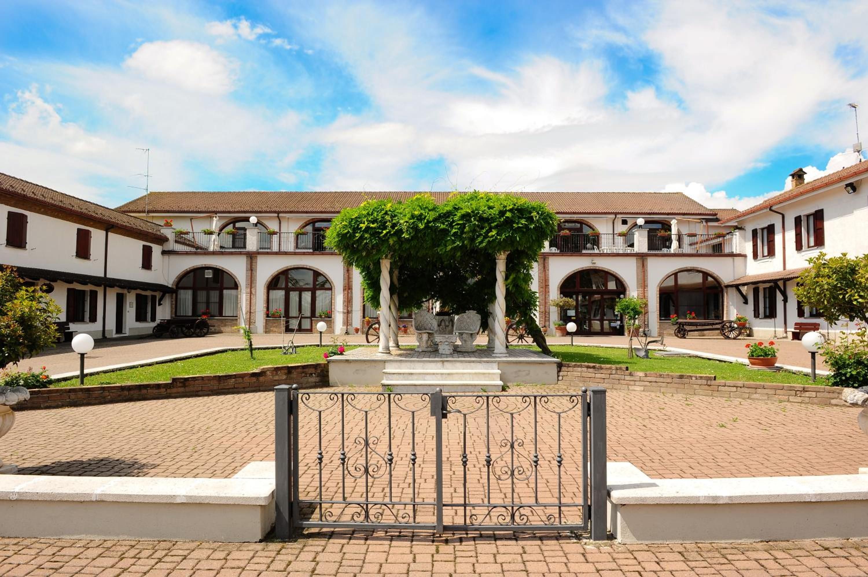 A courtyard with a central fountain, surrounded by white buildings with arched windows and a tiled roof.