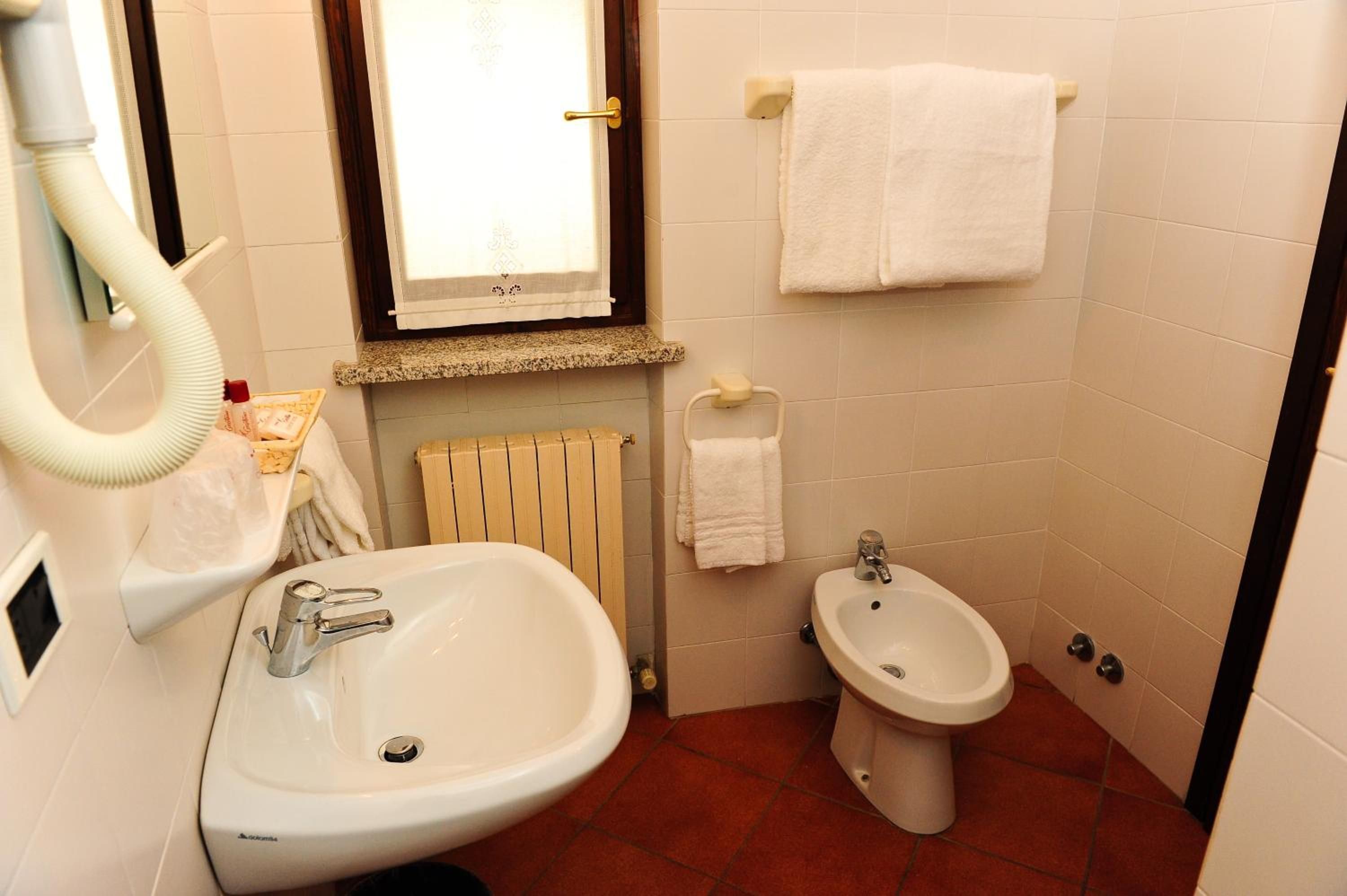 A bathroom with a sink, bidet, towel rack, and a window.