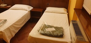 Une chambre d’hôtel avec deux lits simples, une table de chevet avec un téléphone et un radiateur posé sur le sol.