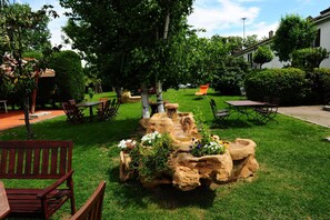 Un jardin bien entretenu, agrémenté d’un massif rocheux central, entouré de différents espaces aménagés pour s’asseoir et avec un bâtiment visible au fond.