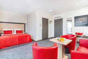 A hotel room with a bed, a desk with breakfast, and a red chair.