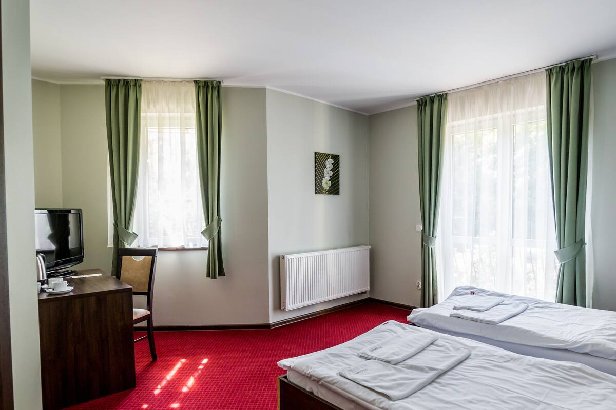 A hotel room with two beds, a desk with a television, and a radiator.