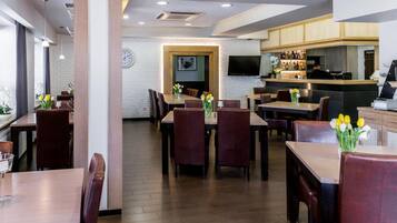 A restaurant with wooden tables and chairs, a bar area, and a clock on the wall.