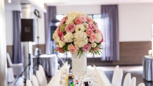 A long banquet table set with white tablecloths, neatly arranged plates, glasses, and a centerpiece of pink and white flowers in a tall vase. - Hotel Walewscy (Gdansk)