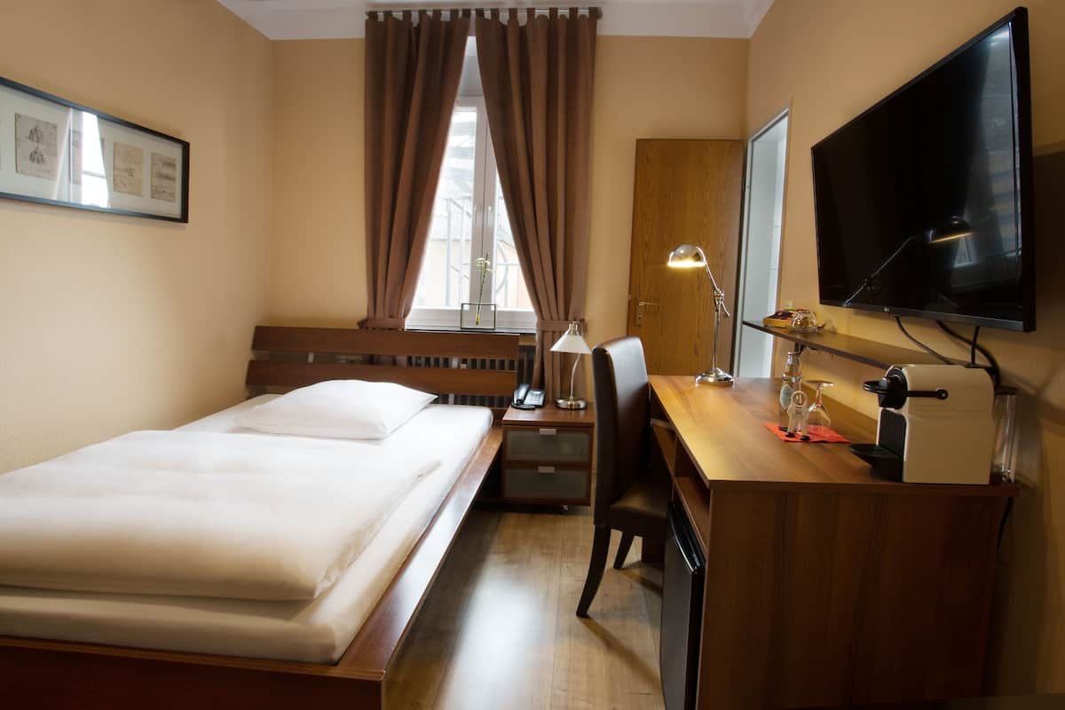 A hotel room with a bed, desk, chair, television, and a window with curtains.