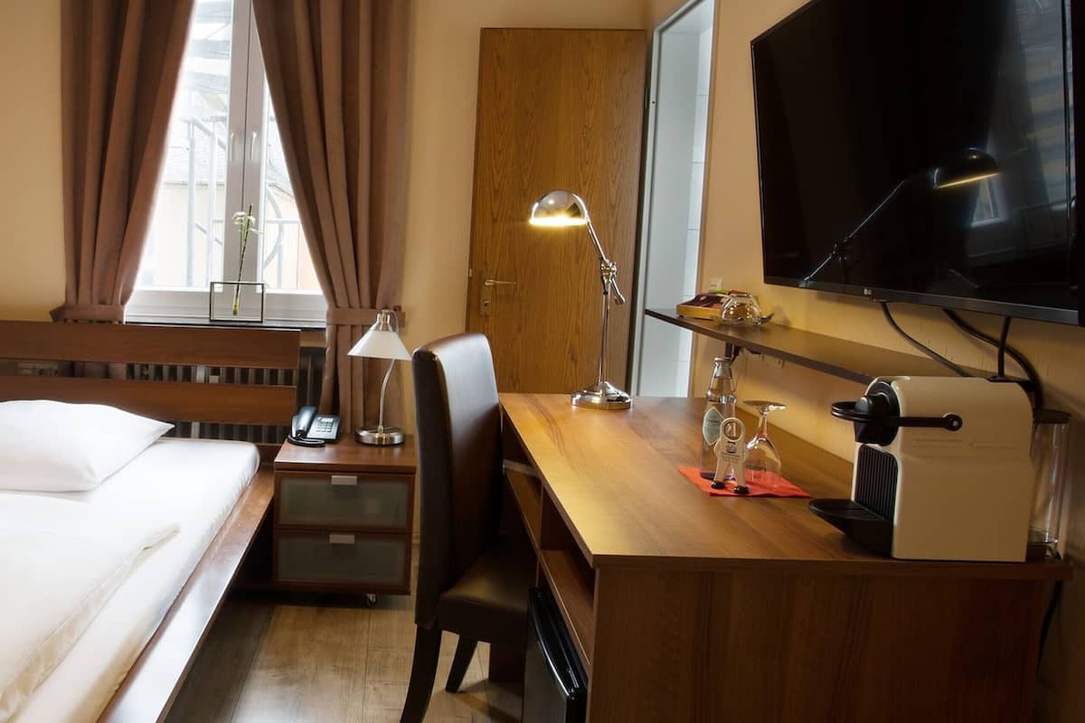 A hotel room with a bed, desk, chair, TV, and a window with curtains.