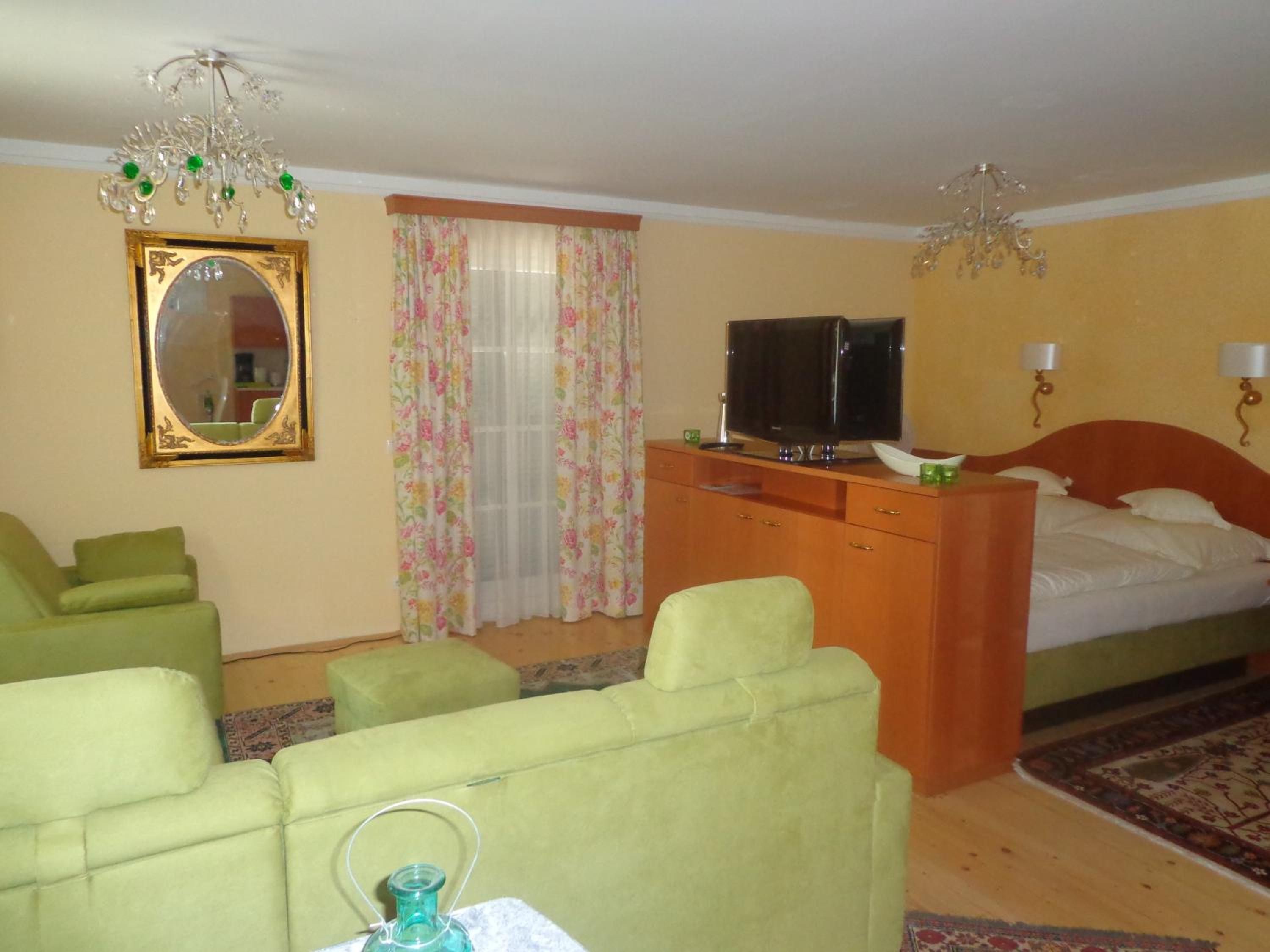 Ein Hotelzimmer mit einem Bett, einem Fernseher, einem Schreibtisch, einem Sessel, einer Couch, einem Spiegel und einer Deckenleuchte.