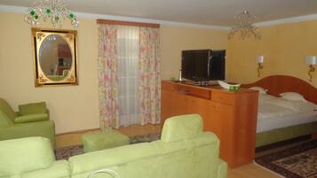 Ein Hotelzimmer mit einem Bett, einem Fernseher, einem Schreibtisch, einem Sessel, einer Couch, einem Spiegel und einer Deckenleuchte.