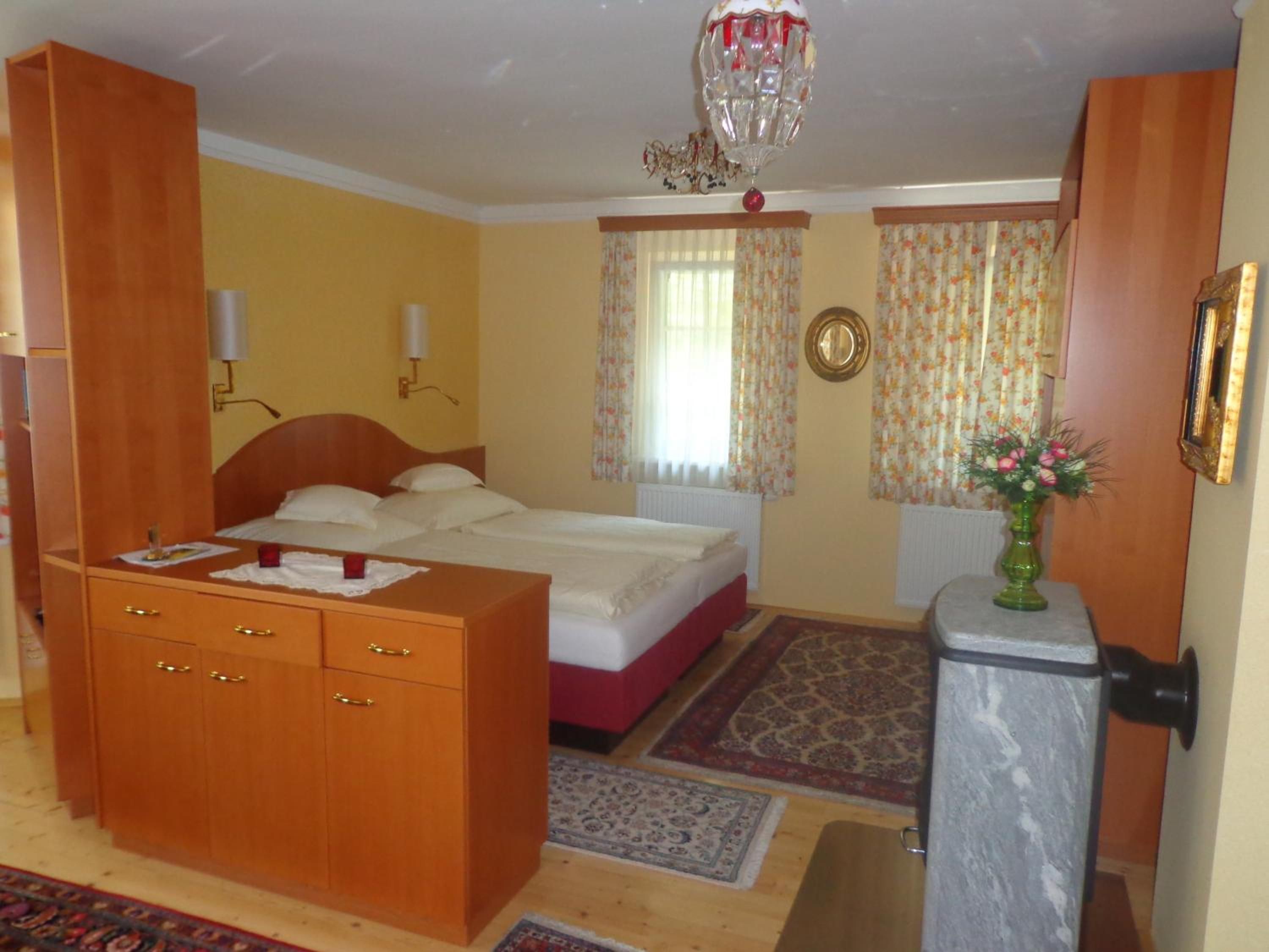 Une chambre à coucher comprenant un lit, une armoire en bois, un bureau, une chaise, un vase avec des fleurs, un miroir et un lustre.